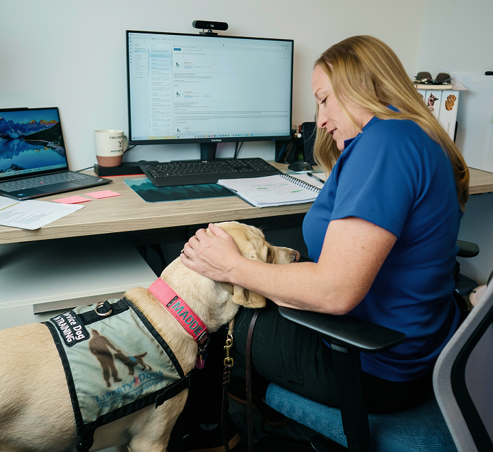 Employee working at a desk with a dog resting nearby.